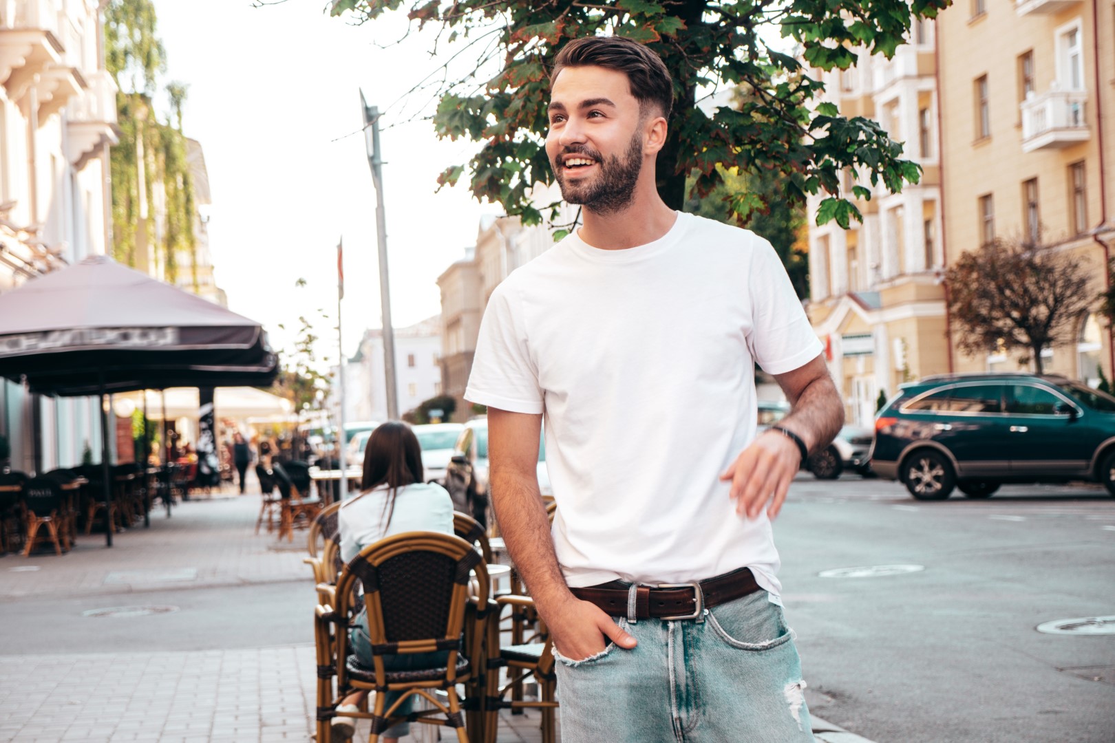 Portrait of handsome smiling stylish hipster model. Man dressed in white T-shirt. Fashion male posing on the street background outdoors at sunny day. Cheerful and happy